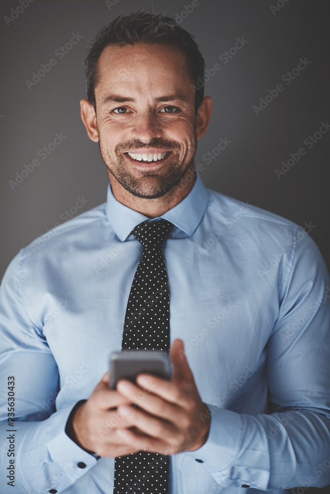 Smiling young businessman using his cellphone against a gray bac