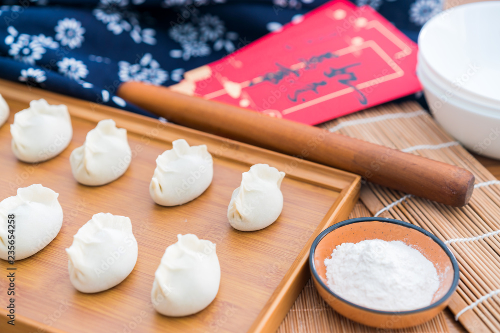 Dumplings, flour, rolling sticks, red envelopes on the wooden table