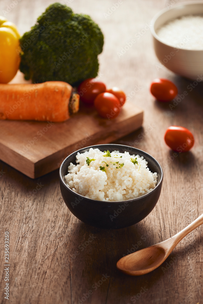 Grains of rice in a wooden bowl and ingredients for a vegetarian recipe - healthy eating concept