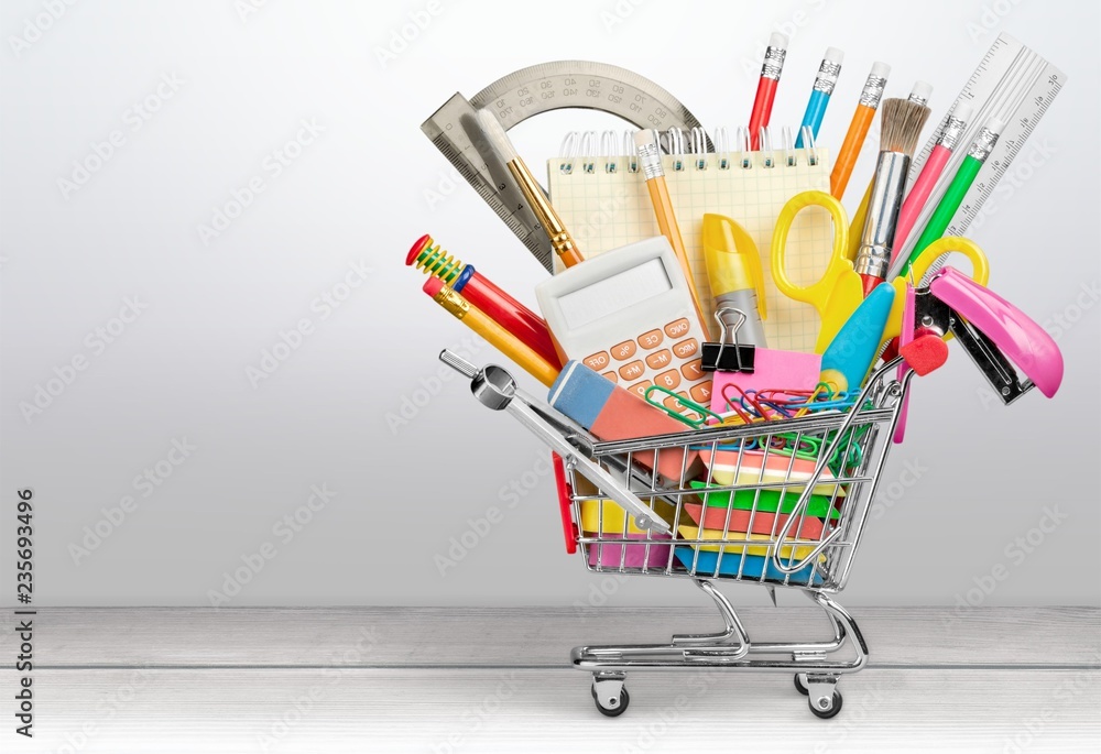 Variety office supplies in little shopping cart on wooden table