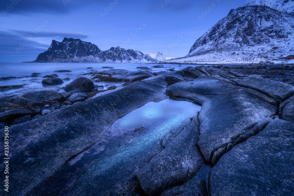 海边有石头和模糊的水，映衬着雪山和黄昏时乌云密布的蓝天。Ut