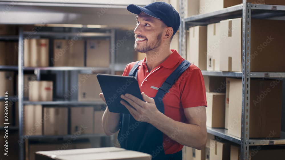 Warehouse Worker Uses Digital Tablet For Checking Stock, On the Shelves Standing Cardboard Boxes.