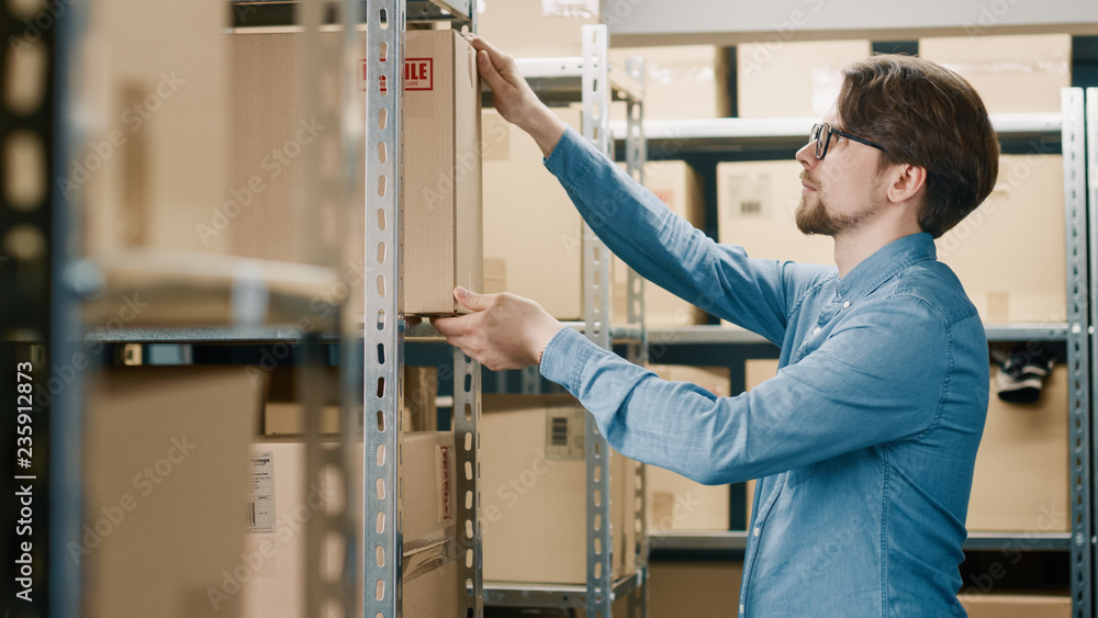 Warehouse Worker Puts Cardboard Box on a Shelf. In the Background Rows of Shelves Full of Cardboard 