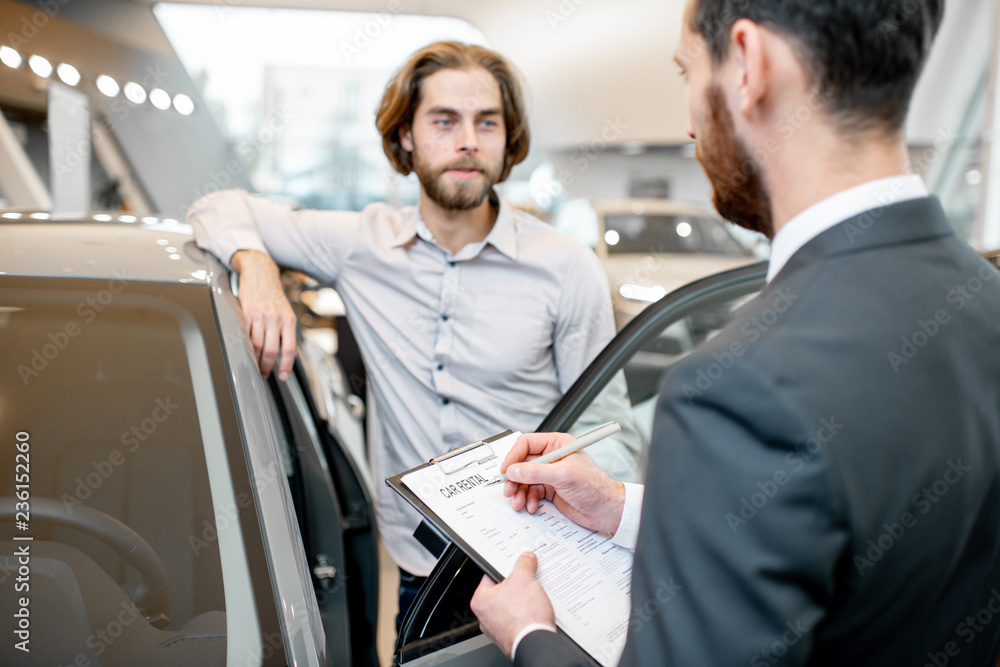 Manager filling car rental documents standing with male client in the showroom