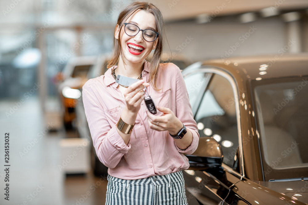 Portrait of a happy woman holding a keychaain of a new luxury car in the showroom