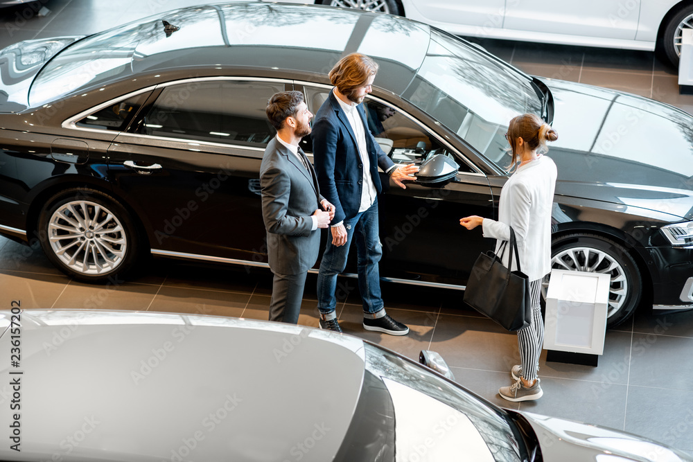 Business couple chosing a new car standing with salesperson in the car showroom. View from above