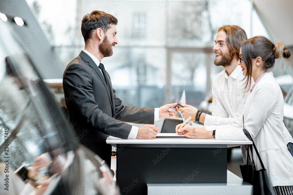 Young business couple signing some documents at the table with salesperson or manager buying or rent