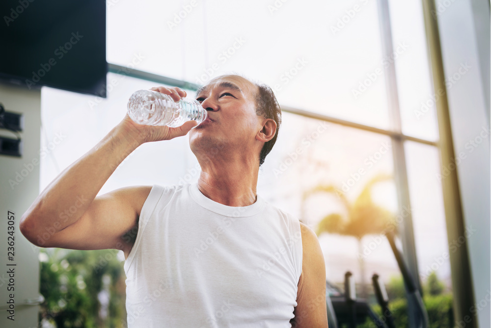 老年人运动后在健身房健身中心喝矿泉水。老年人健康的生活方式。