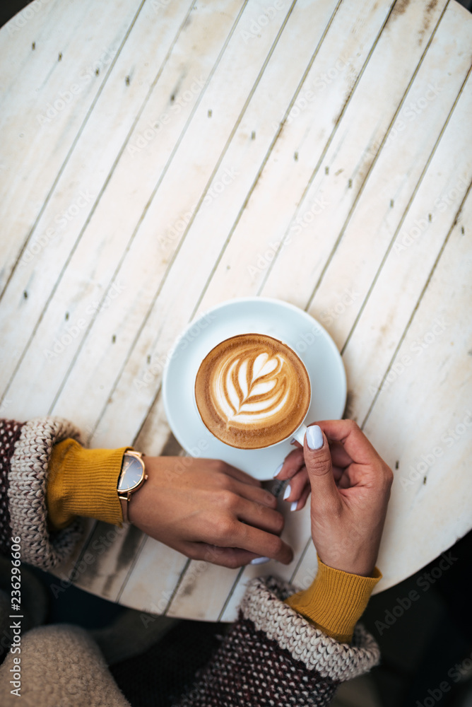 Top view of young woman holding a cup of coffee with latte art.