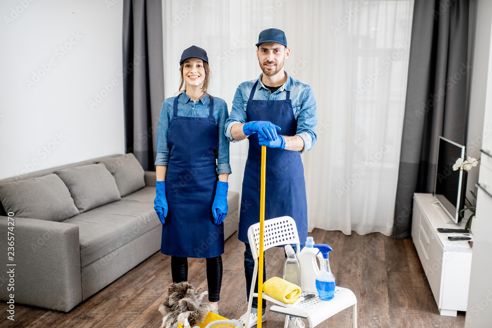 Portrait of a young couple as a professional cleaners in blue uniform with cleaning tools in the apa