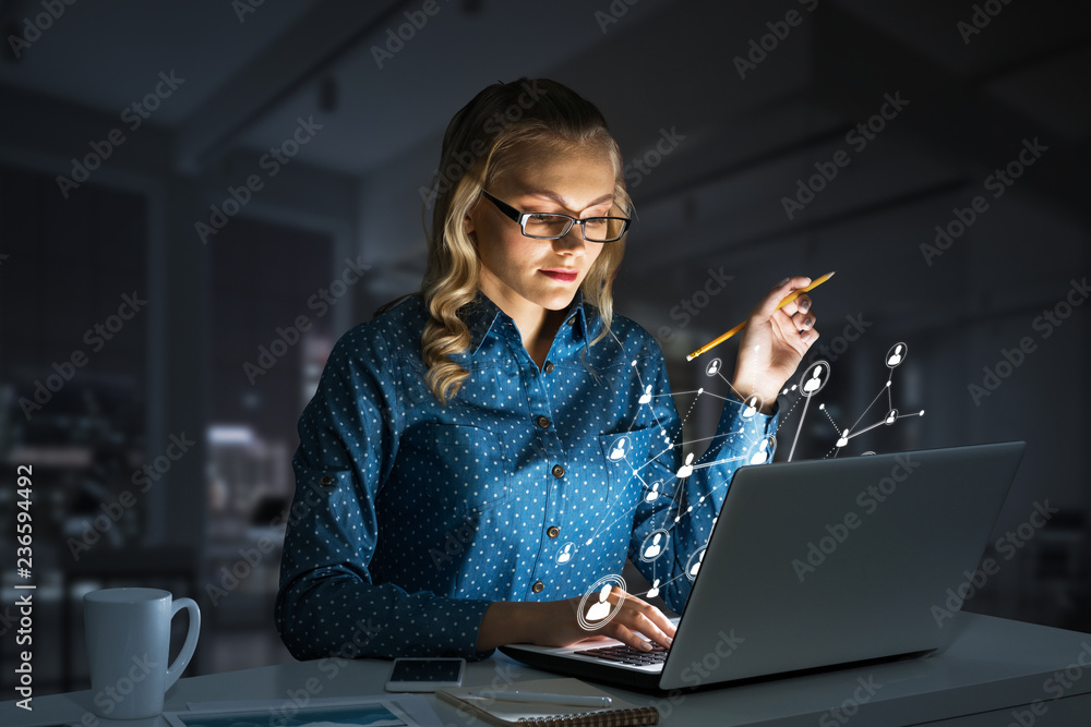 Attractive blonde wearing glasses in dark office using laptop. Mixed media