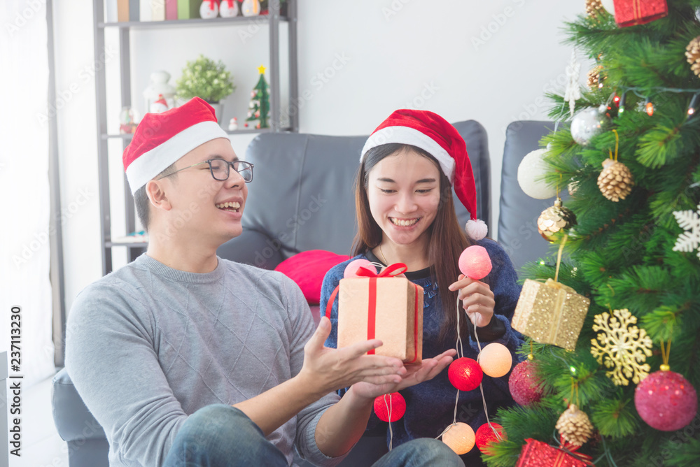 美丽的亚洲女孩和男朋友戴着圣诞老人帽在家装饰圣诞树度假