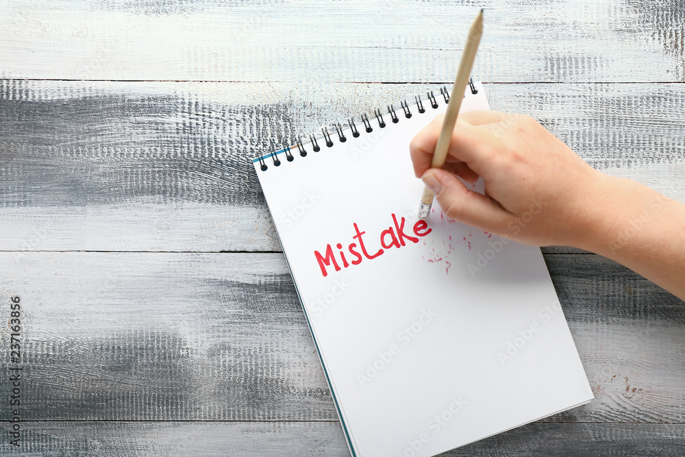 Woman erasing text MISTAKE written in notebook, top view