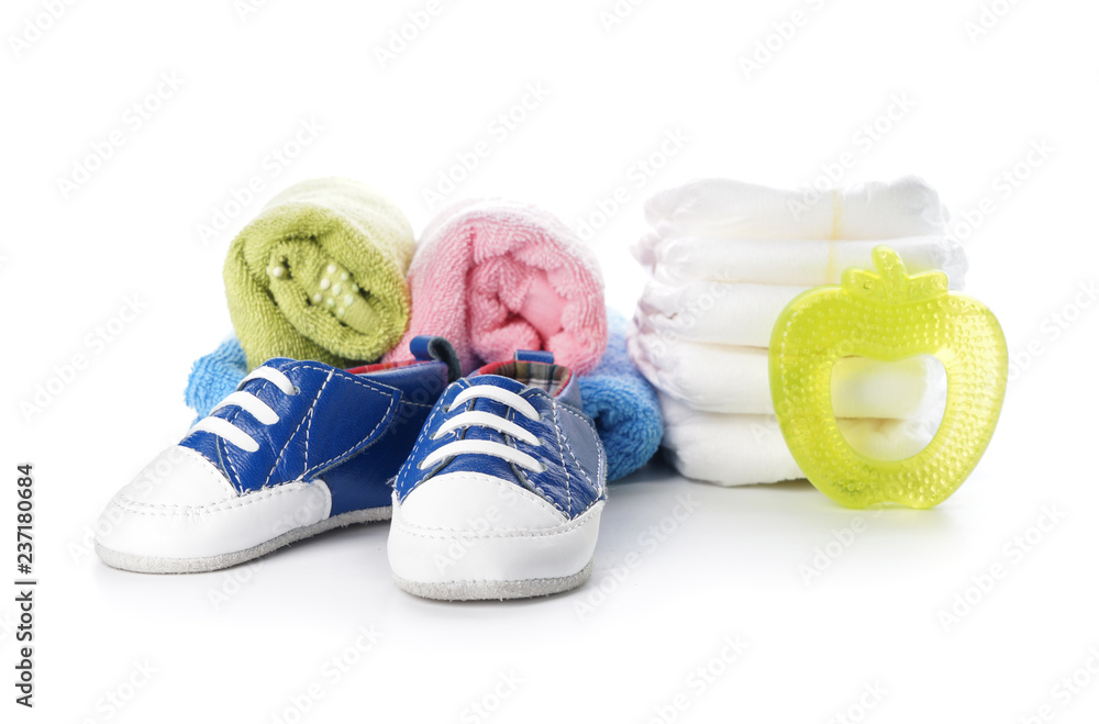 Shoes with stack of diapers with towels and baby teether on white background