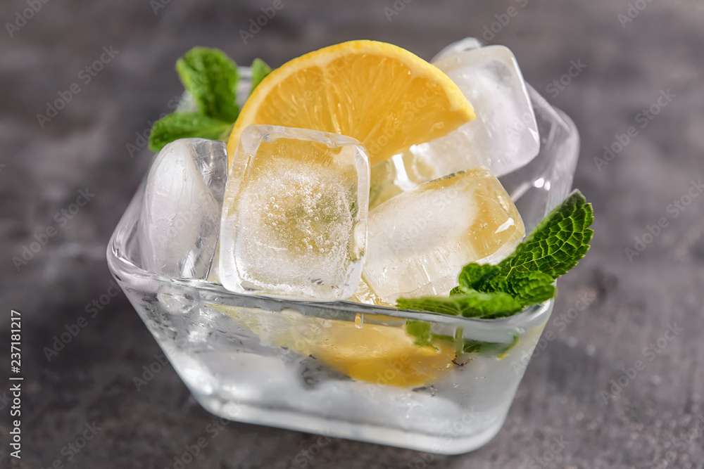 Bowl with sliced lemon and ice cubes on grey table