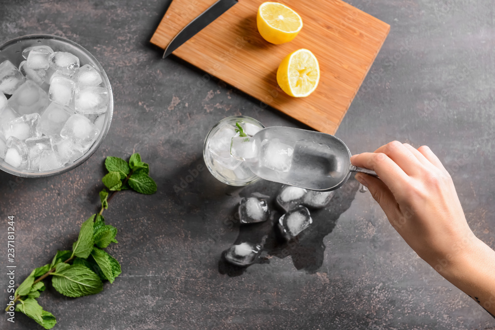 Woman putting ice cubes into glass on grey background