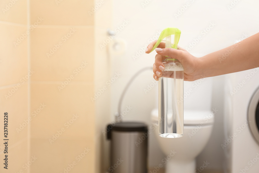 Woman holding spray air freshener in bathroom