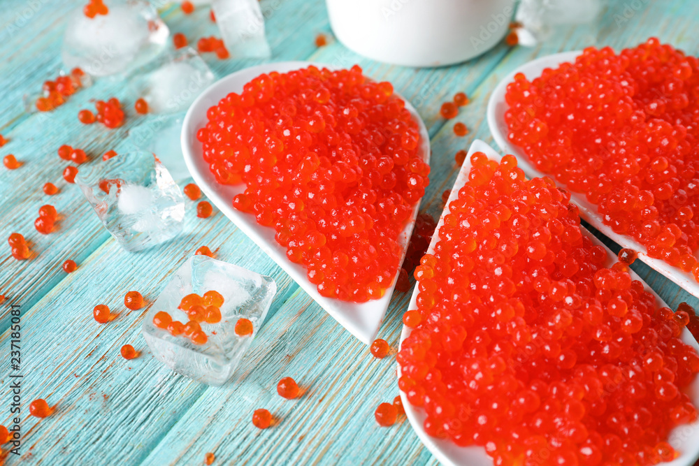 Plates with delicious red caviar on color wooden table