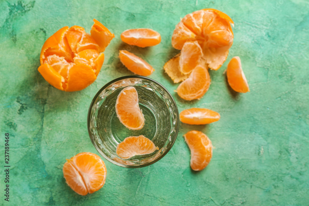 Glass of fresh water with tangerines on color table