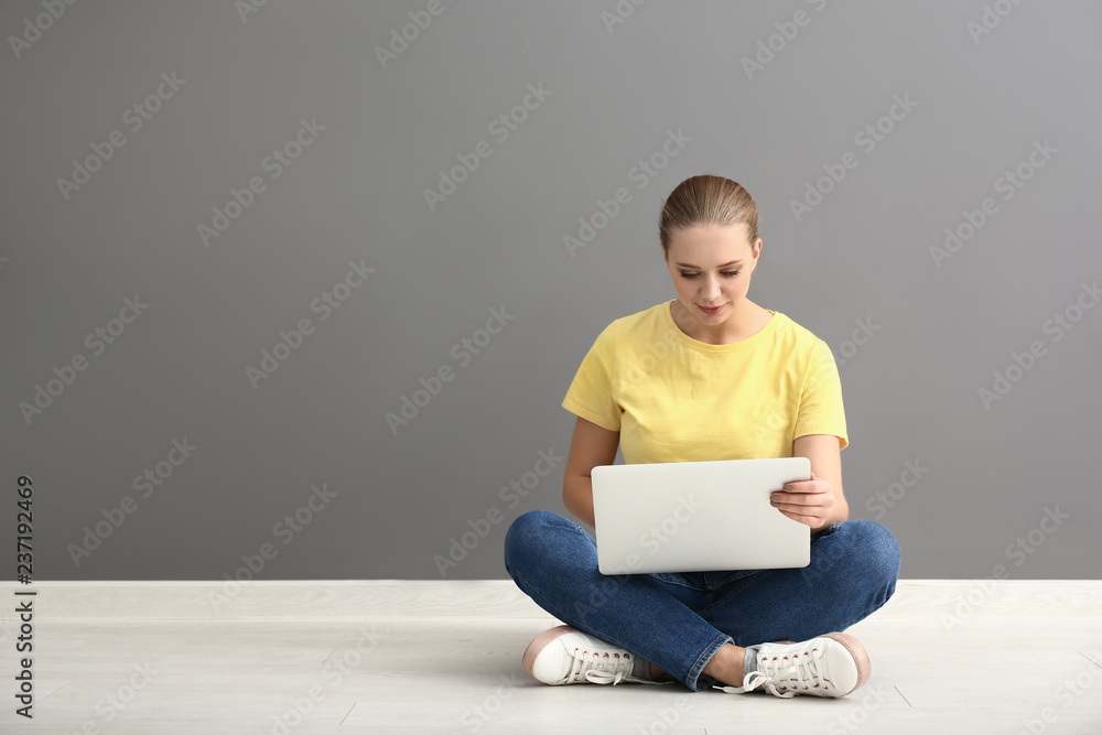 Female student with laptop sitting near grey wall