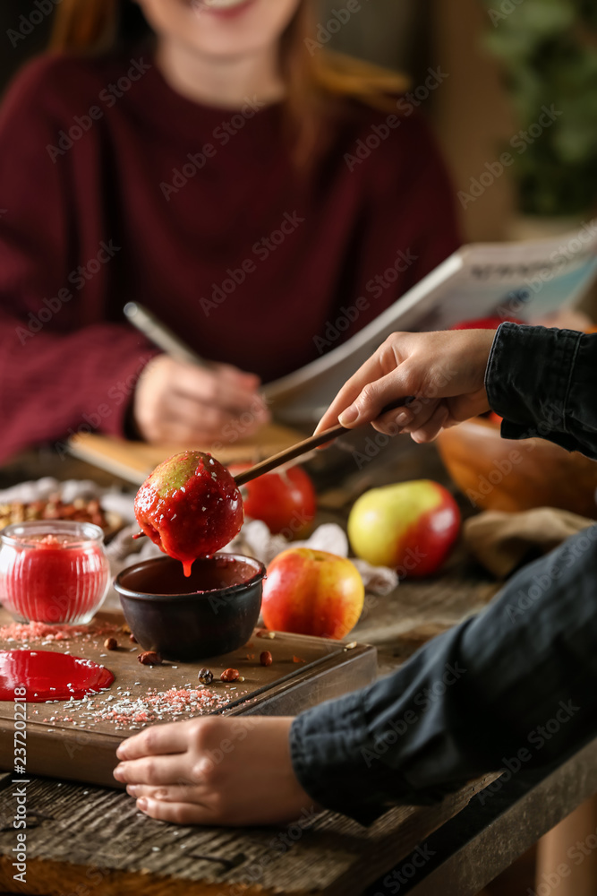 Woman dipping apple into bowl with caramel on wooden table