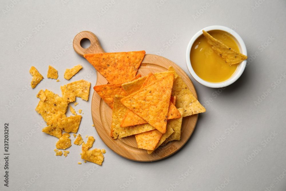 Wooden board with tasty corn chips and sauce on grey background