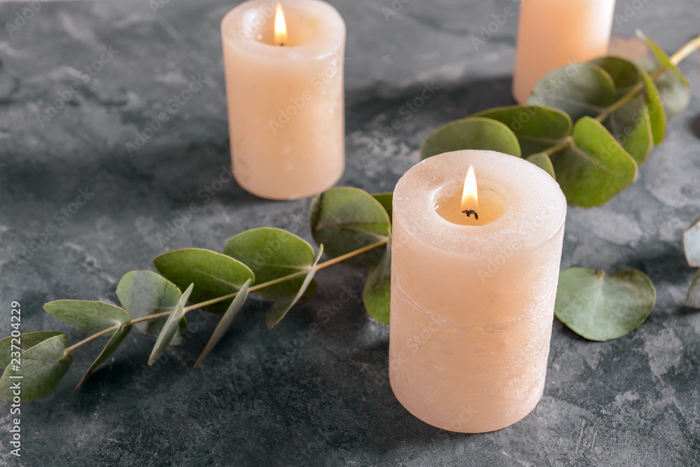 Burning candles with eucalyptus branches on grey table