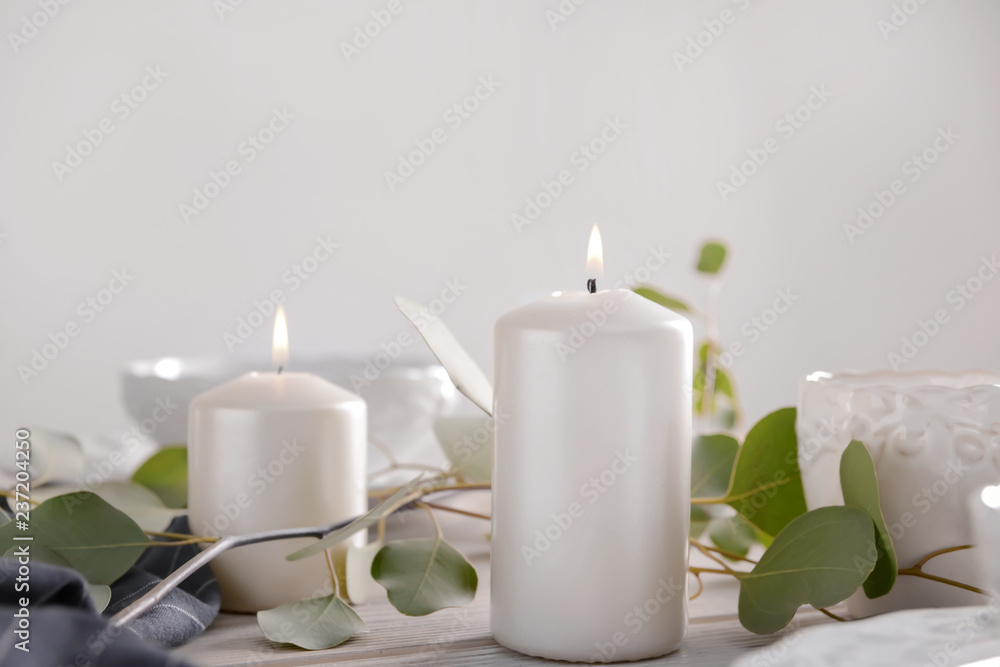 Burning candles with eucalyptus branches on wooden table