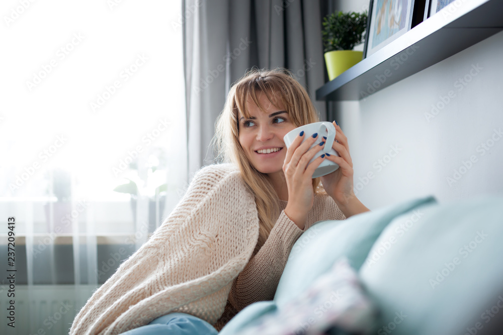 Happy woman in soft sweater relaxing at home with cup of hot tea or coffee