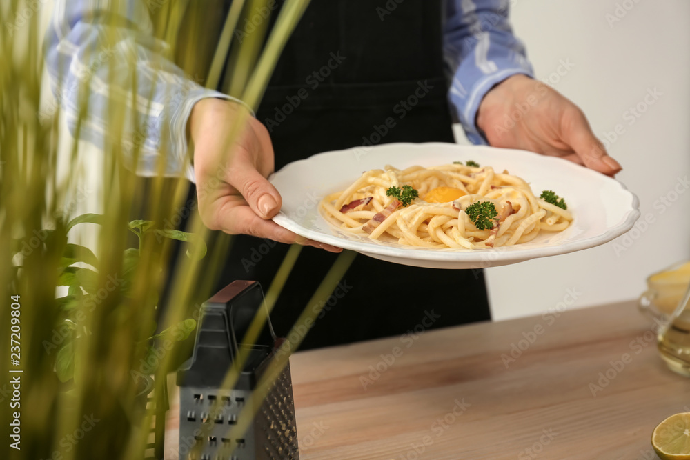 Woman holding plate with delicious pasta carbonara in kitchen