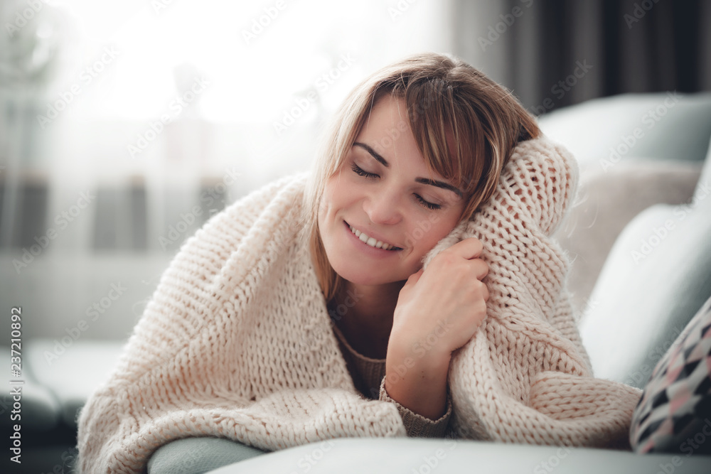 Happy young woman hugging soft knitted sweater, relaxing on sofa at home