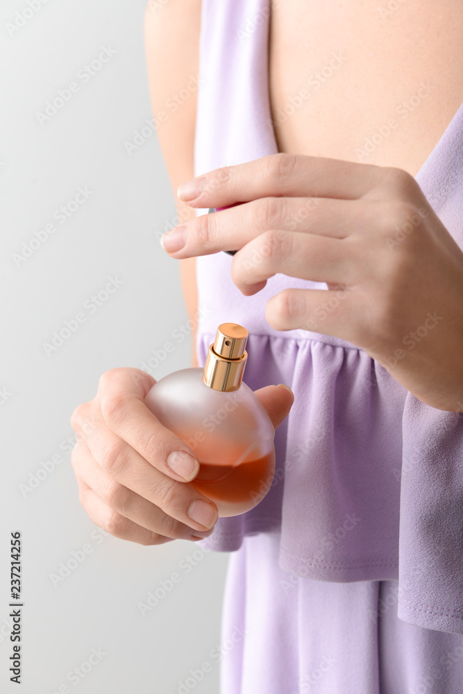 Woman with bottle of perfume on grey background, closeup