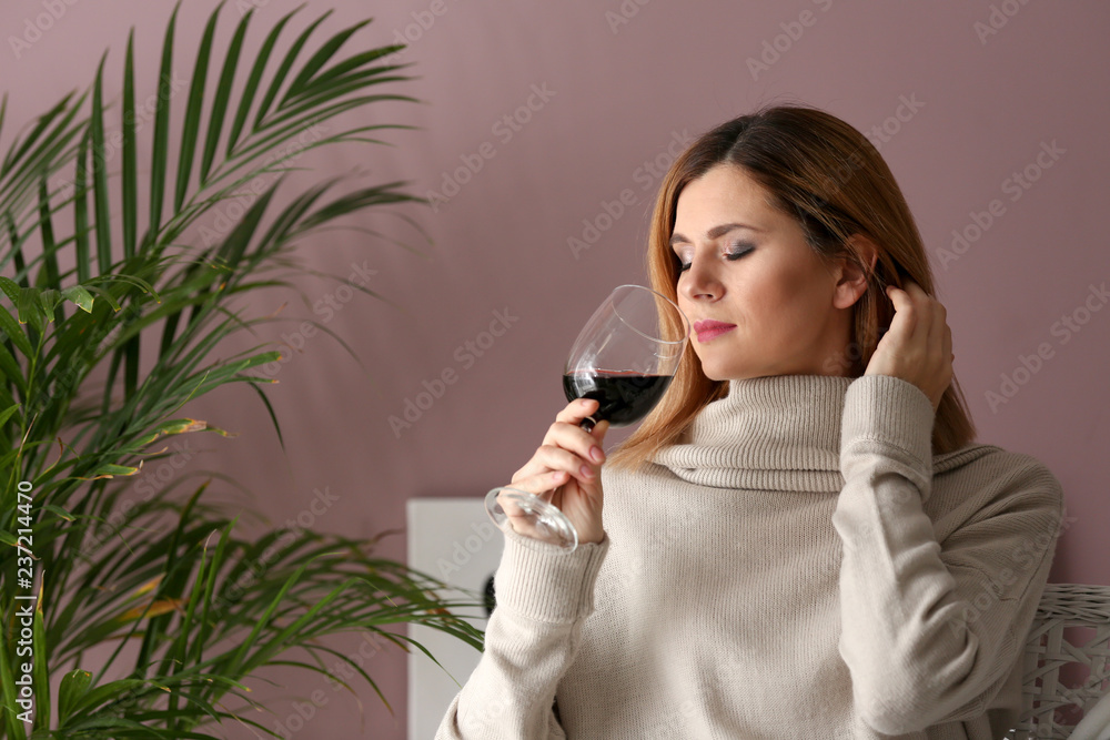 Beautiful woman smelling tasty wine at home