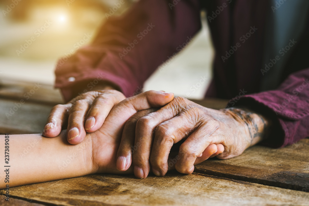 Hands of the old man and a childs hand on the wood table