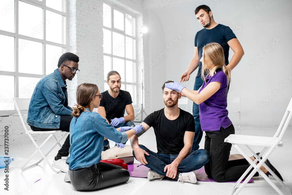 Group of young people during the first aid training with instructor showing how to tie a bandage on 