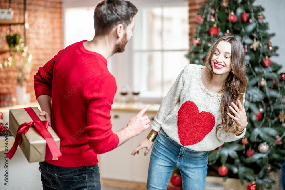 Man holding a gift behind for a young woman celebrating New Year holidays at home