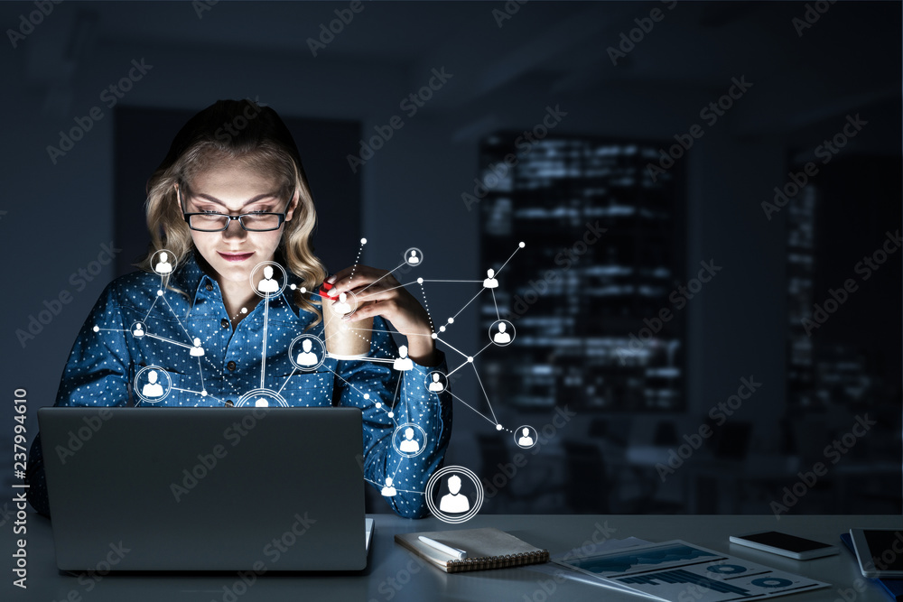 Attractive blonde wearing glasses in dark office using laptop. M