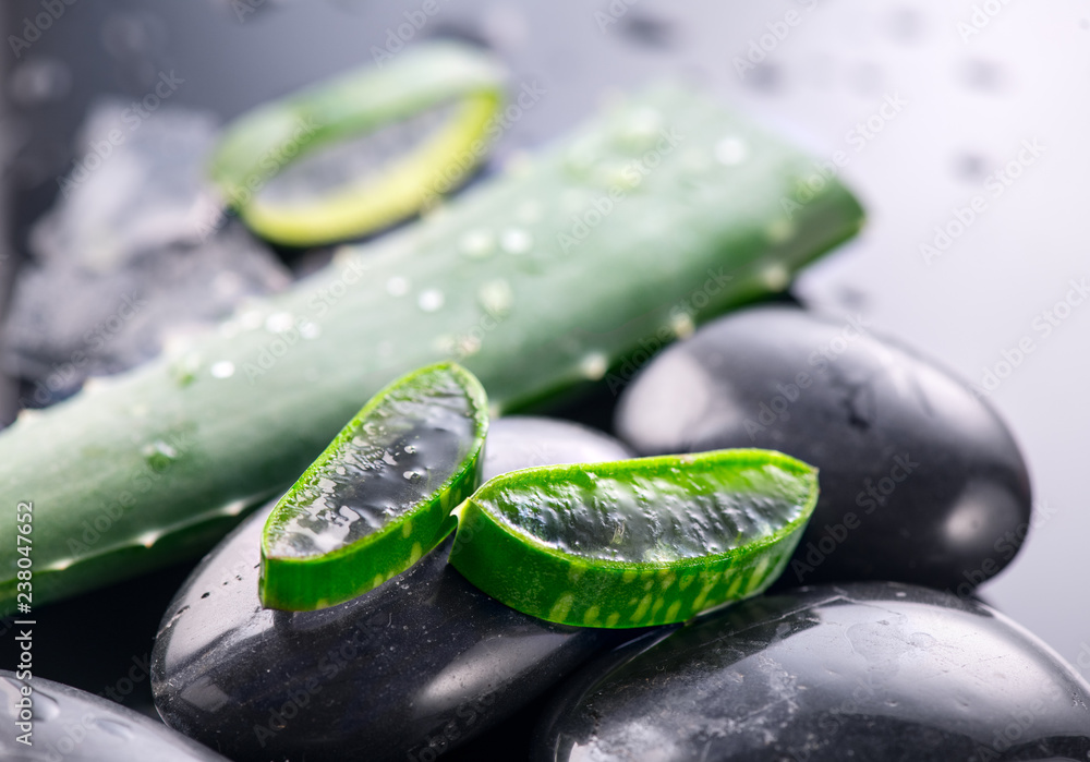 Aloe Vera slices and spa stones closeup on black background. Aloevera plant leaf gel, natural organi