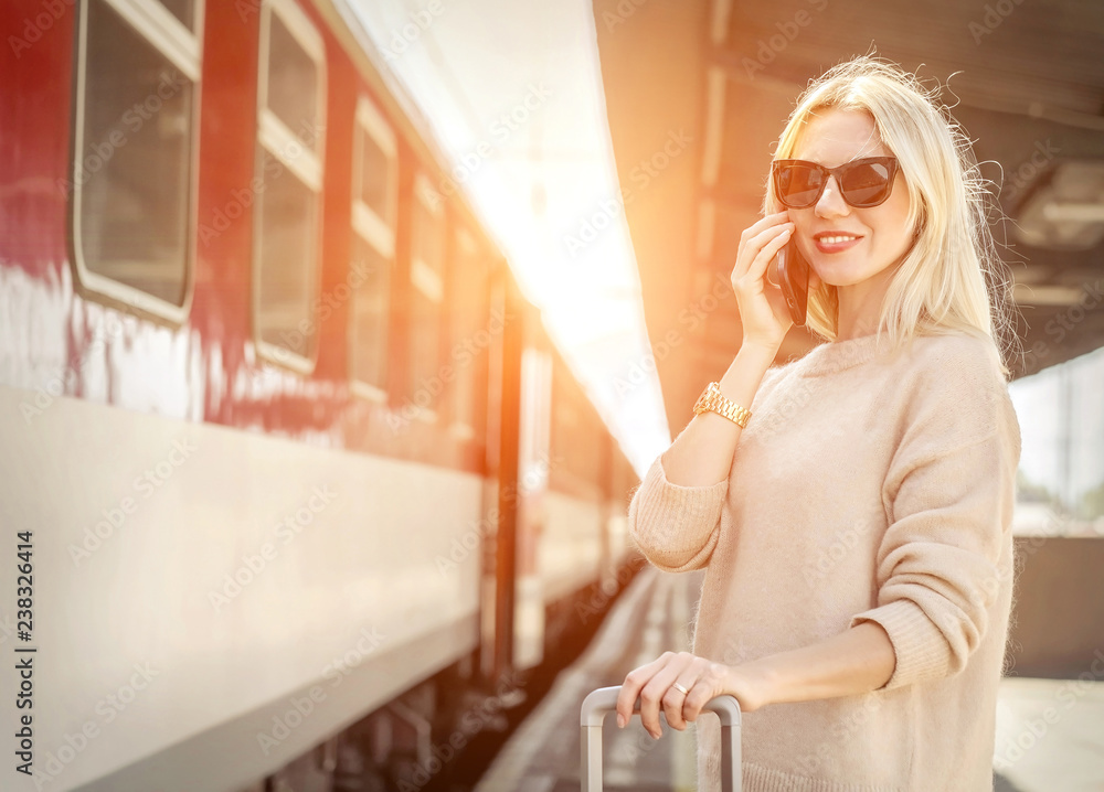 Blonde woman with her luggage stay  and speak in her mobile near train