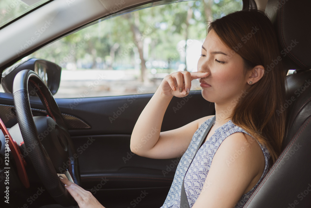 Young woman holding her nose because of bad smell in car.