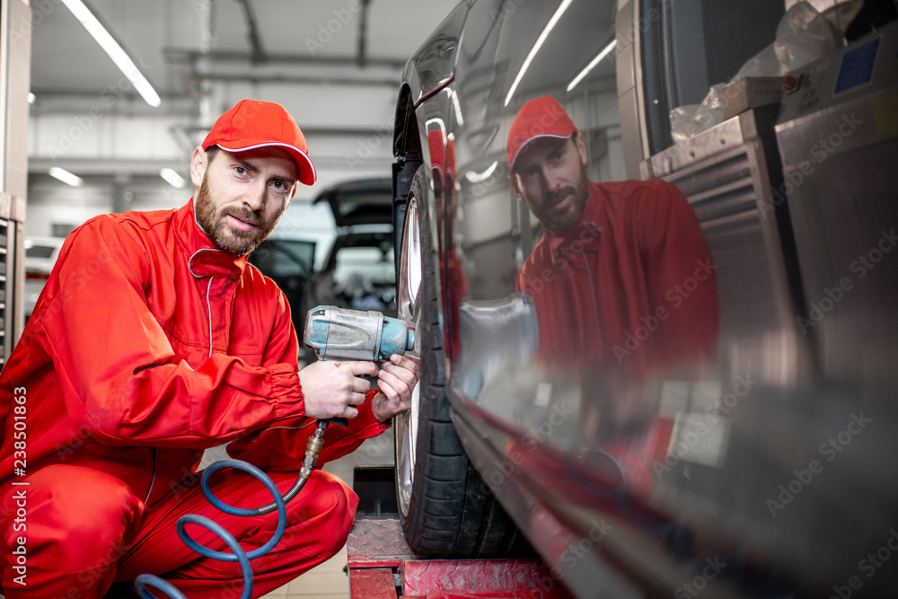 Car service worker in red uniform changing wheel of a sport car at the tire mounting service