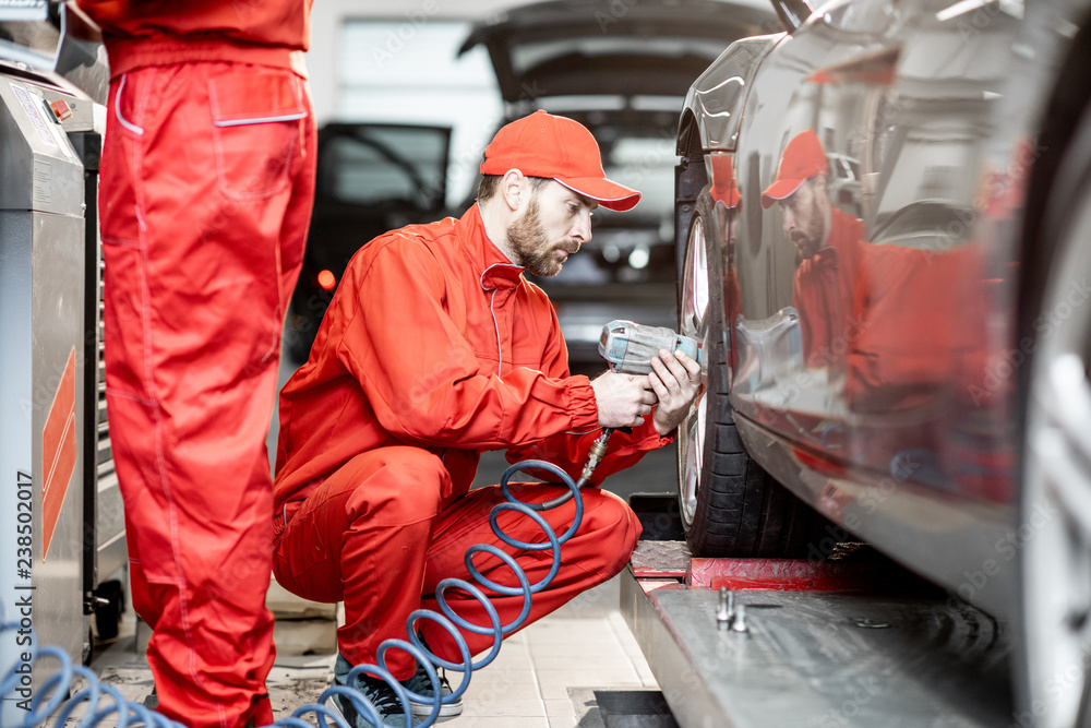 Two car service workers in red uniform changing wheel of a sport car at the tire mounting service