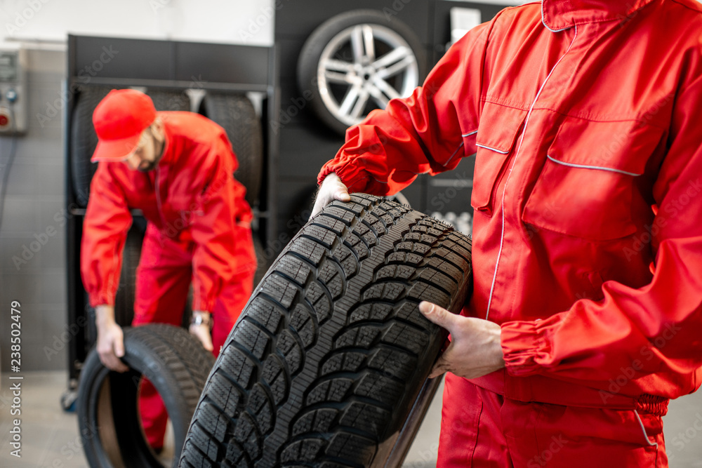 Worker in uniform carrying new tires at the car service or store, close-up view