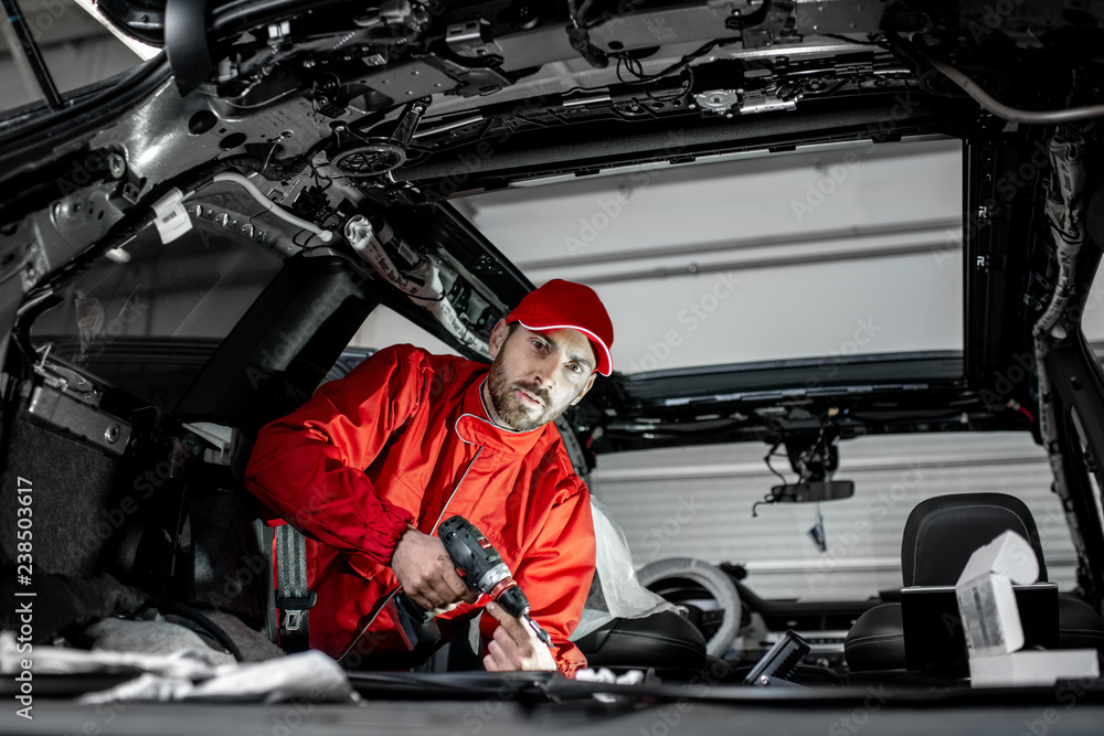 Handsome auto service worker in red uniform disassembling new car interior making some improvements