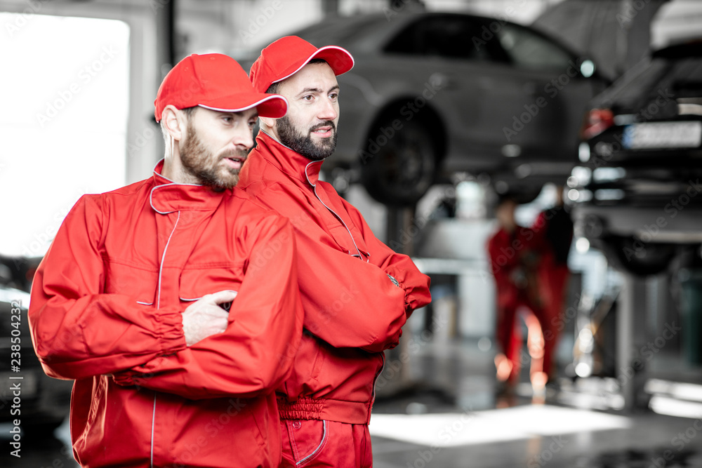 Portrait of a two handsome auto mechanics in red uniform standing together at the car service