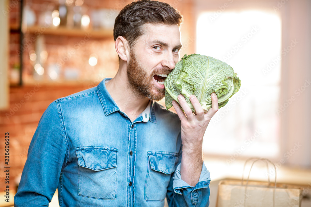 一个英俊的男人拿着卷心菜头在厨房里的肖像。健康的素食概念