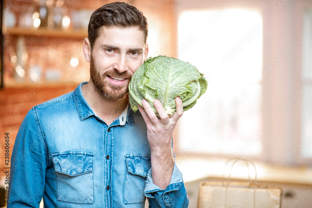 一个英俊的男人拿着卷心菜头在厨房里的肖像。健康的素食概念