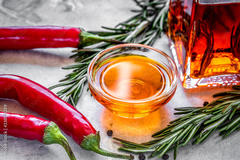 Bottle with chili oil and herbs on stone background