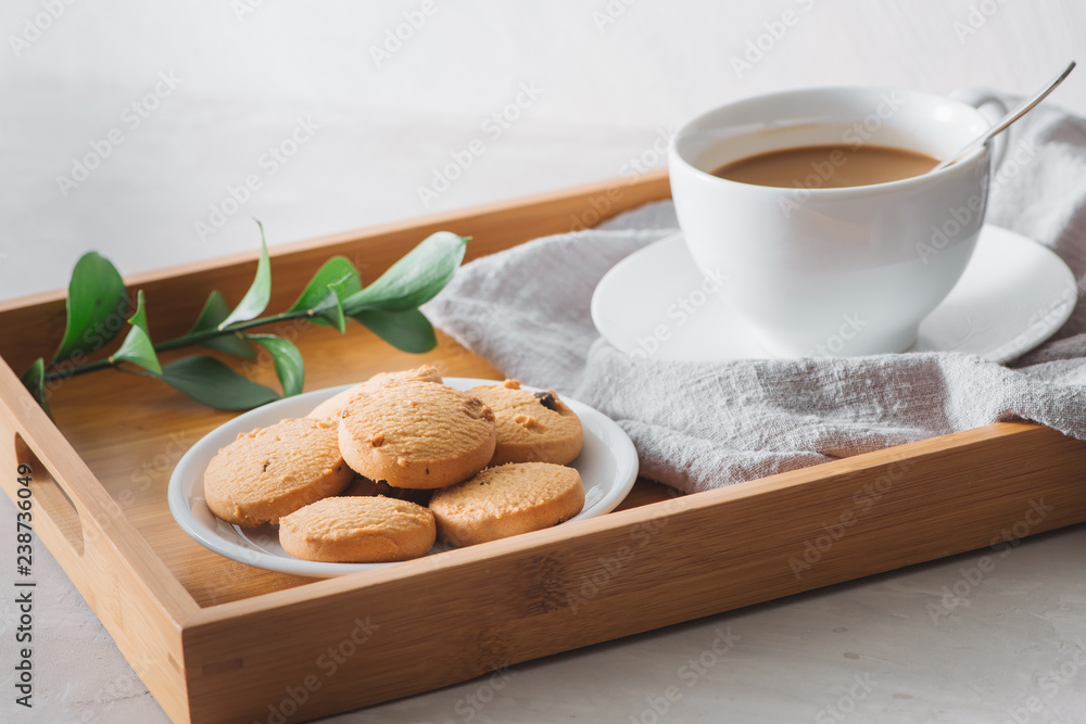 白色杯子里有牛奶和美味饼干的咖啡特写。在浅色石头背景上拍摄