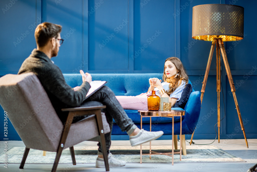 Young woman visiting male psychologist lying on the comfortable couch during psychological session i